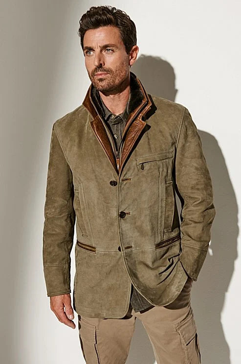 Man in an olive-green suede jacket with tan leather lapels, worn over a dark shirt and beige cargo trousers, hand in pocket. 1
