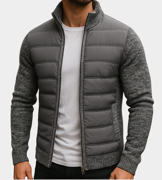 Man wearing the quilted jacket in dark grey with marl knit sleeves and ribbed collar, unzipped over a white t-shirt. 1