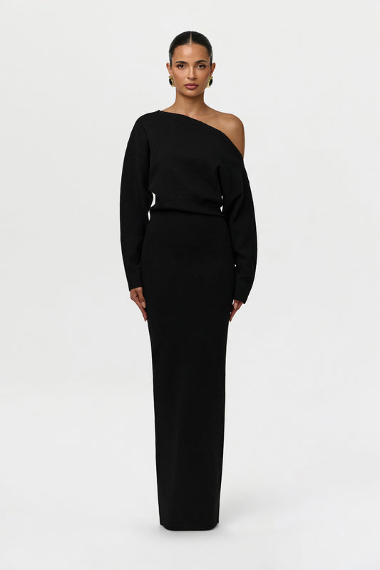 Model facing the camera in a black off-the-shoulder knit maxi dress with long sleeves and a fitted column skirt. 1