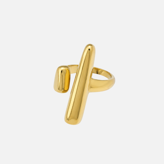 Open gold-toned ring with a long polished bar crossing the band and a small rounded end opposite, on a plain pale background. 1