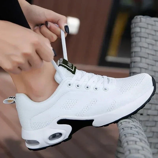 Hands tying the white laces of a white knit trainer with a white air-cushioned sole, worn on a foot outdoors. 1