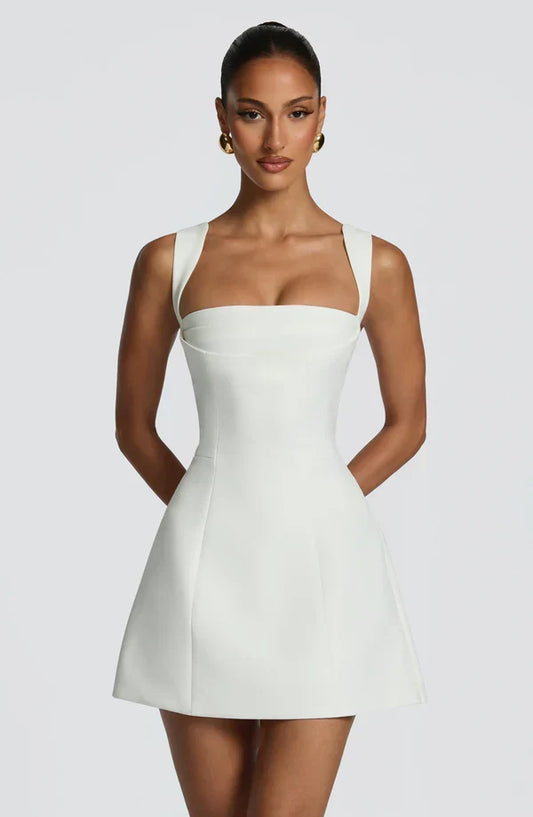 Model faces the camera in the white mini dress, showing the square neckline, wide straps and fitted corset bodice above a flared skirt. 1