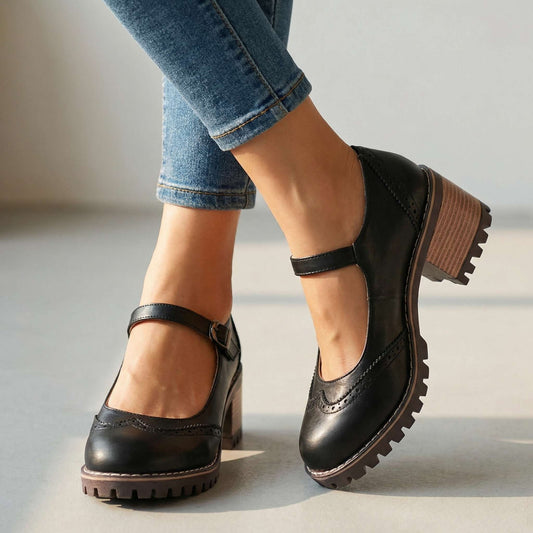Black brogue-detail shoes with buckled ankle strap and chunky stacked heel, worn with rolled blue jeans in a bright indoor setting. 1