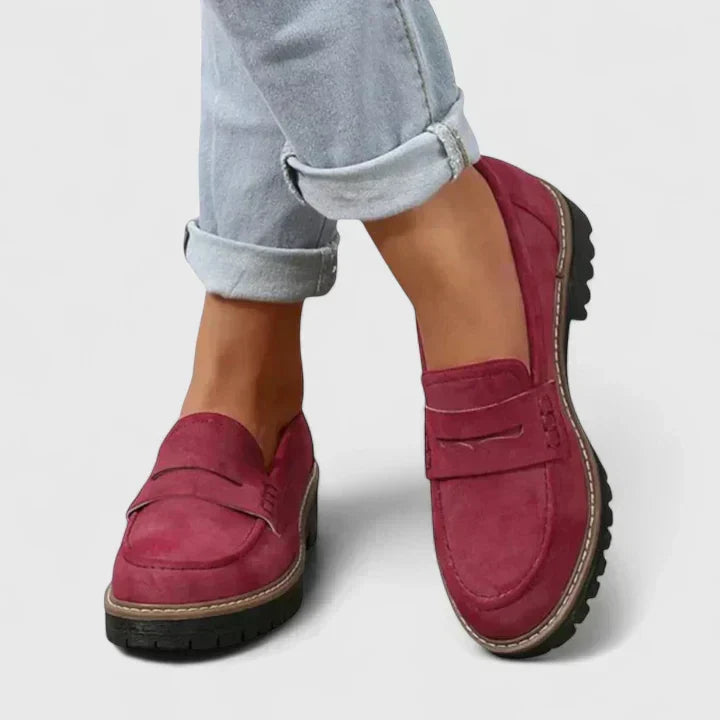 Burgundy red loafers worn with rolled light grey jeans, showing the penny strap and treaded black sole. 6