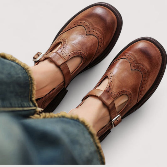 Top-down view of tan brogue Mary Janes with buckled T-straps worn with frayed-hem blue jeans. 1