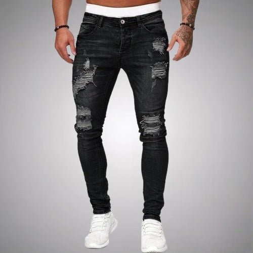 Front view of slim-fit ripped jeans in washed black, worn by a model with white trainers, showing knee and thigh distressing. 1