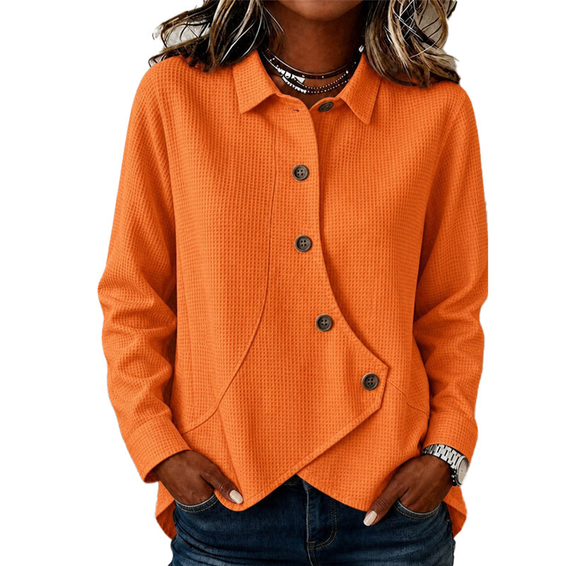 Model wearing the waffle-knit jumper in orange, hands in jeans pockets, showing the collar, brown buttons and curved asymmetrical hem. 4