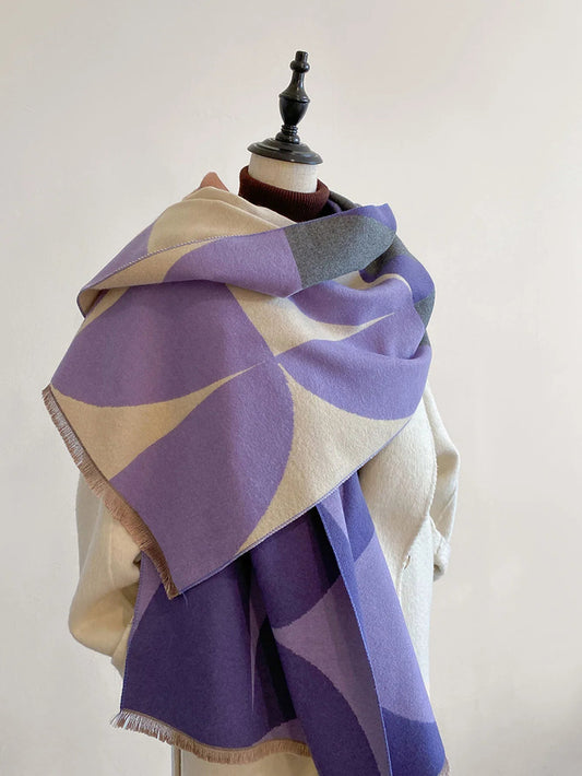 Scarf in purple, cream and grey geometric curves draped over a mannequin's shoulders, with a cream coat and fringed ends. 1