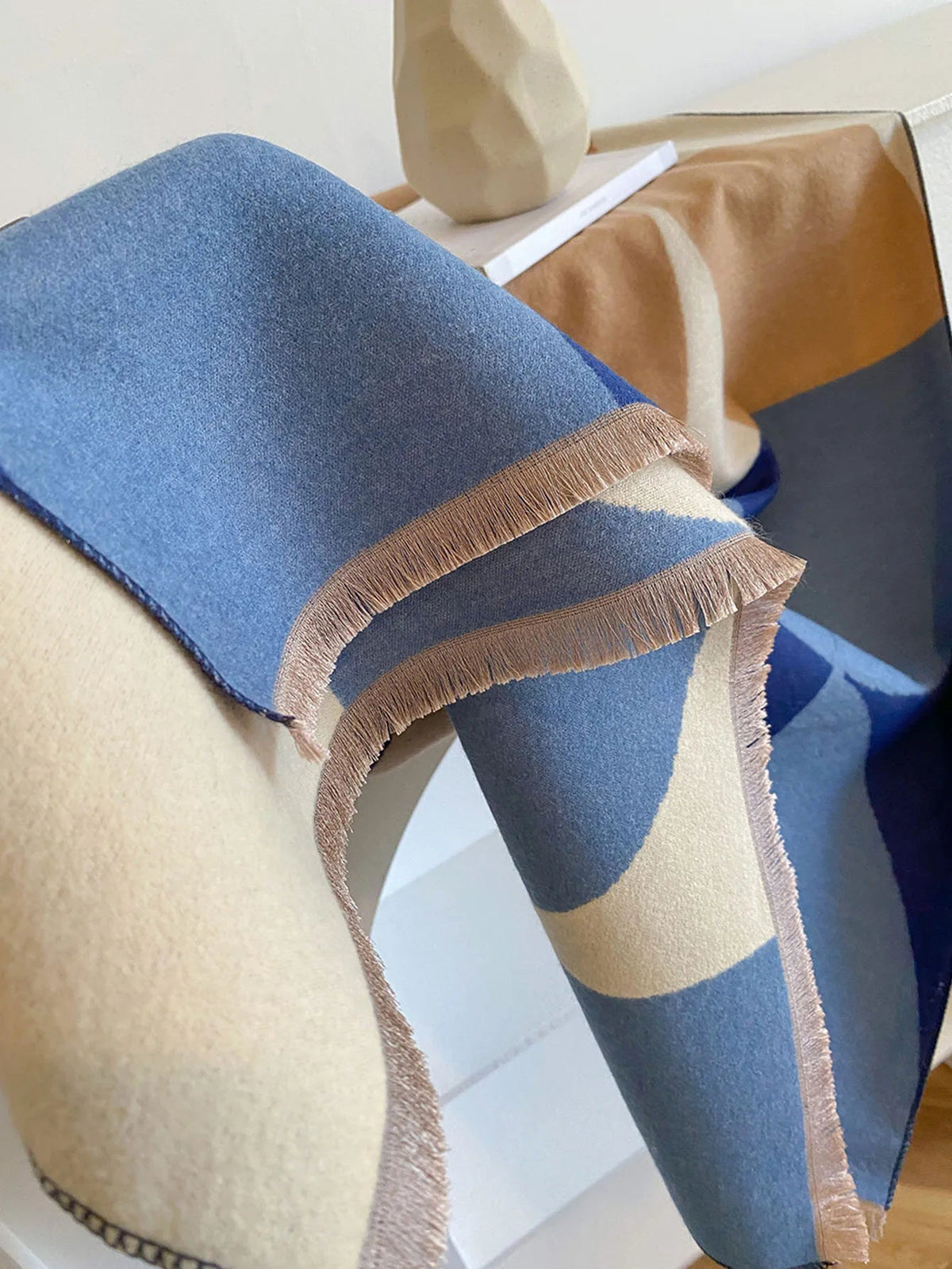 Close-up of the blue and cream scarf folded over a shelf, showing the double layers of fabric and tidy fringe. 12