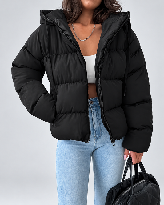 Black quilted puffer jacket worn open over a white crop top and light blue jeans, with a black bag in hand. 1