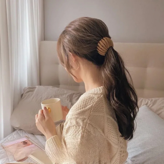 Woman seen from behind holding a mug, wearing a pale gold ribbed clip to hold her low ponytail in place. 2