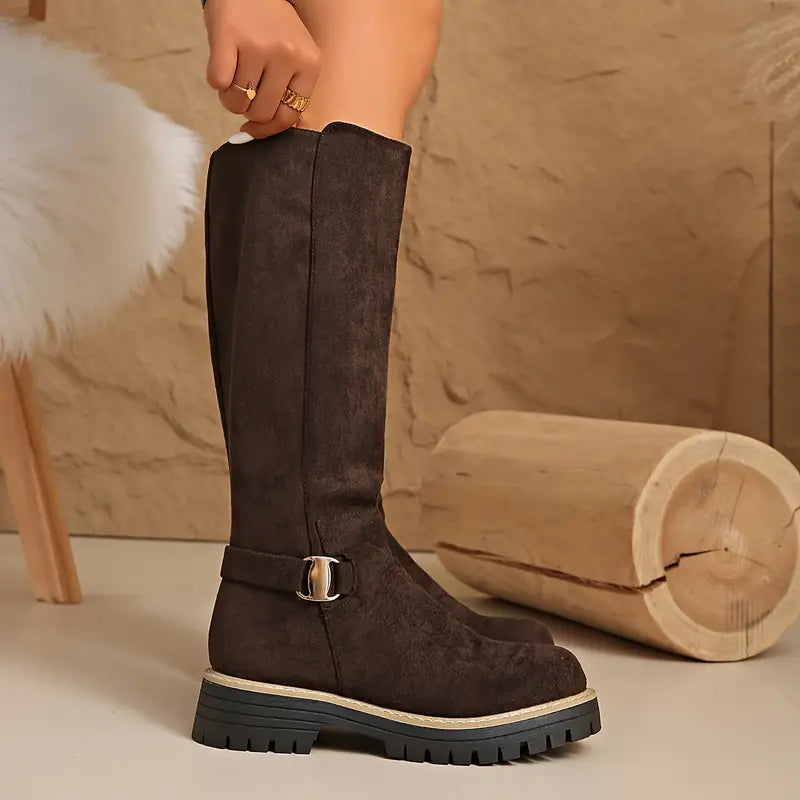 Side view of a dark brown tall boot on a model's leg, showing the gold buckle strap and thick black treaded sole. 7