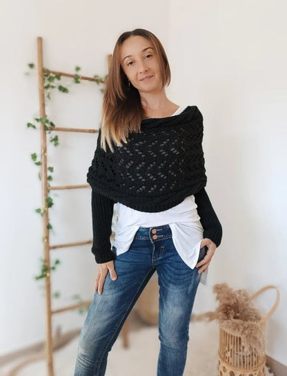 Black lace-knit wrap with built-in sleeves worn over a white top and jeans, model standing front-on beside a ladder. 12
