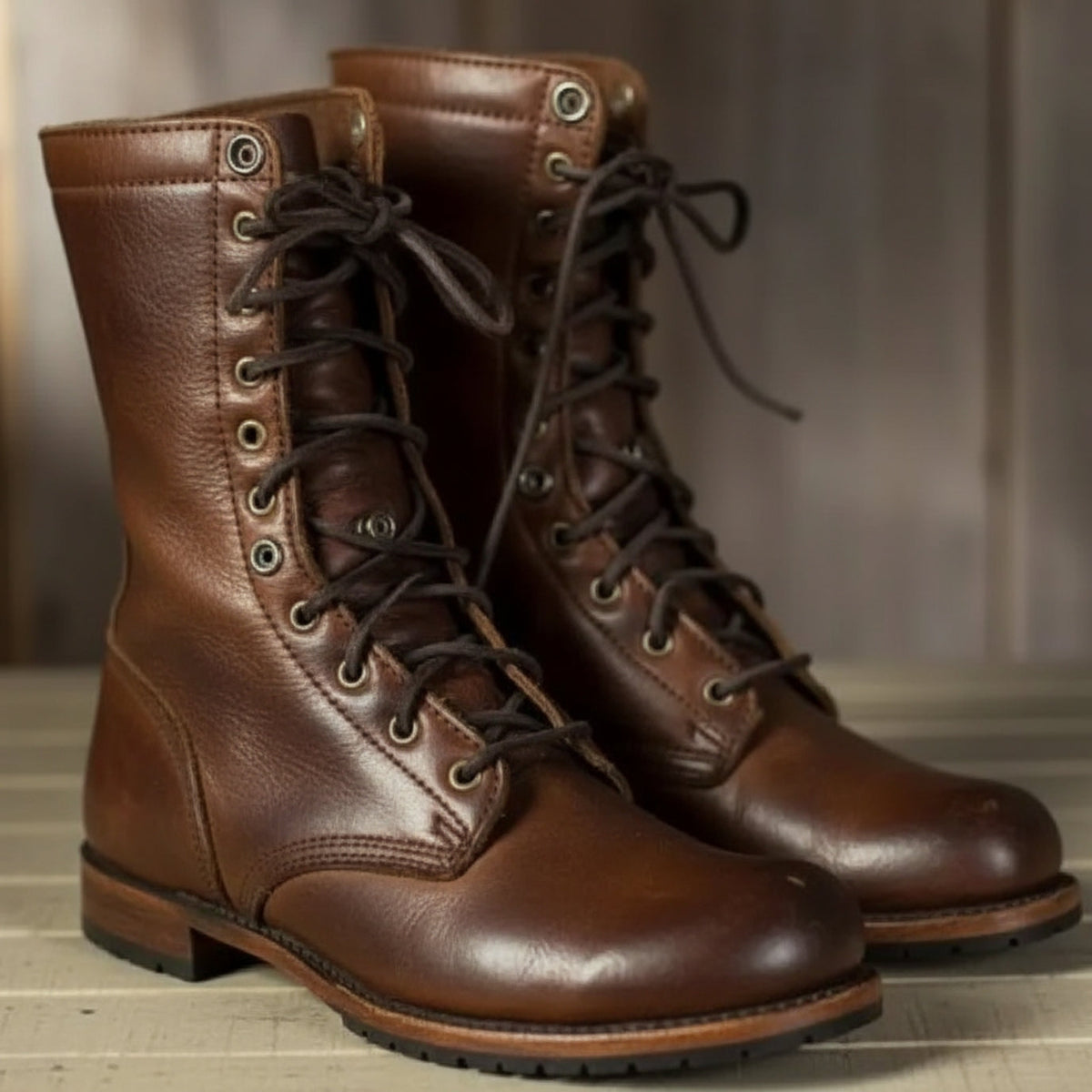 Pair of brown leather lace-up boots with dark laces and metal eyelets, standing side by side on a pale wooden surface. 1
