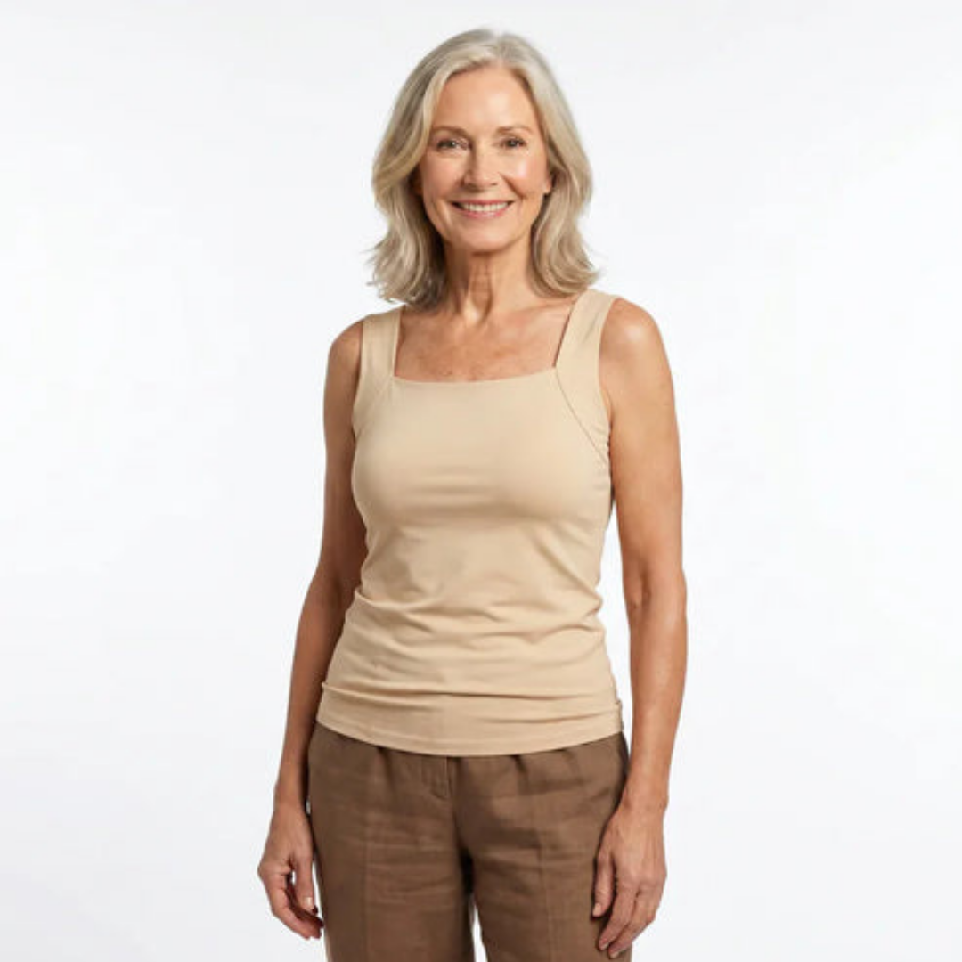 Smiling grey-haired woman wearing a fitted beige square-neck vest top with wide straps and brown linen trousers, front view on white. 1