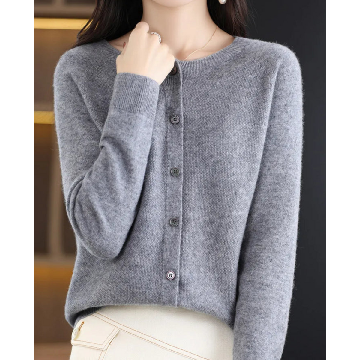 Grey marl cardigan on a model with one hand at her collar, showing the round neck, ribbed cuffs and grey buttons. 7