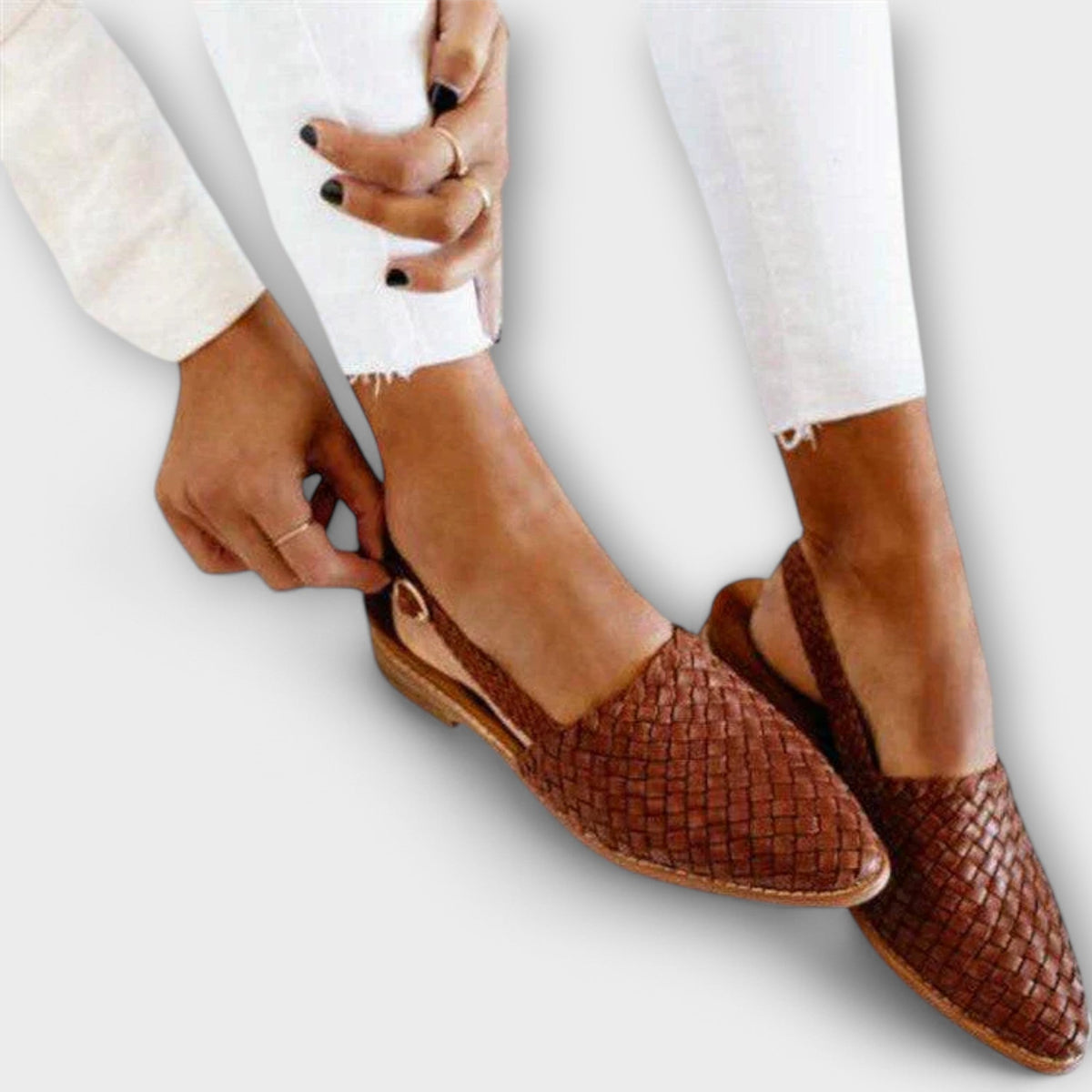 Tan woven slingback flats on a model in white frayed jeans, her hand fastening the buckled heel strap. 1