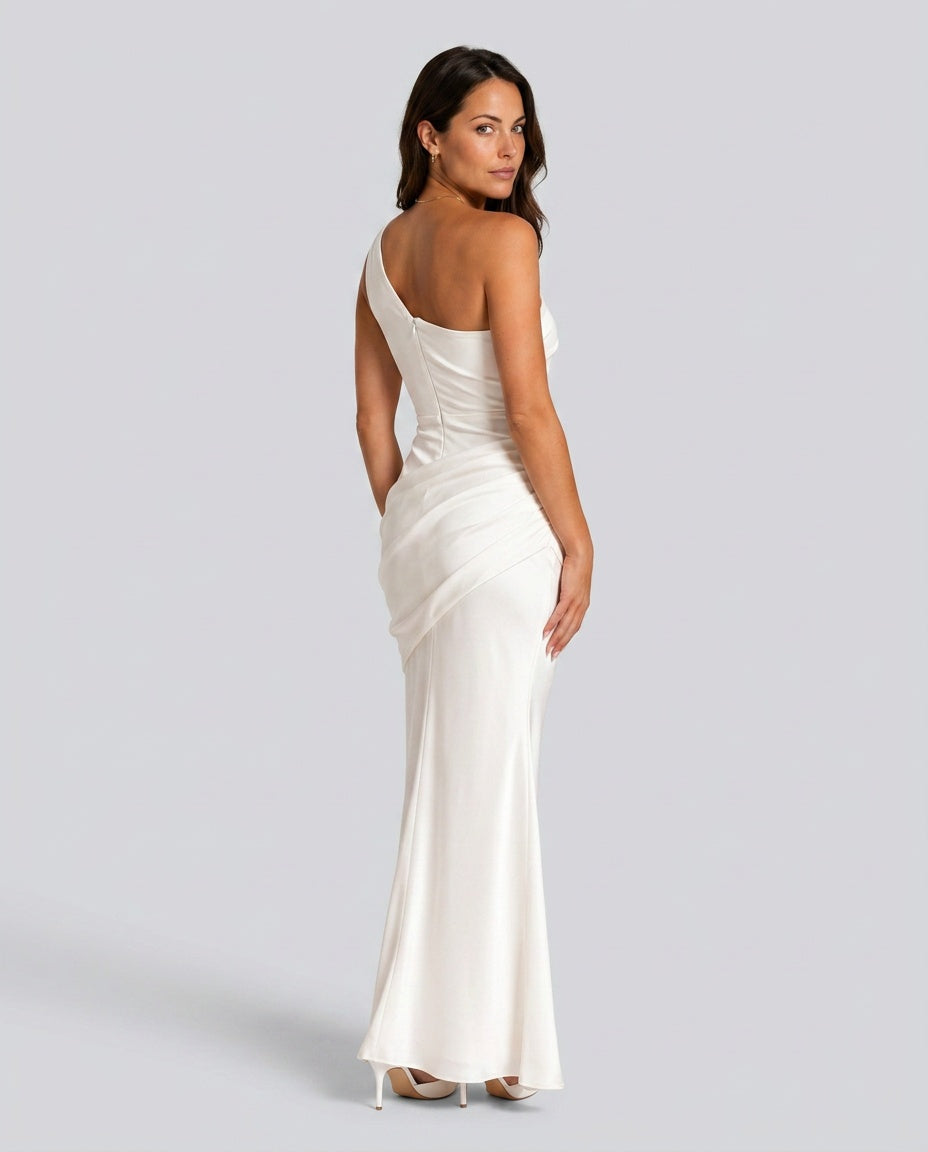 Back view of the ivory dress, showing the one-shoulder back with a side zip and draped hip, worn with white heels. 4