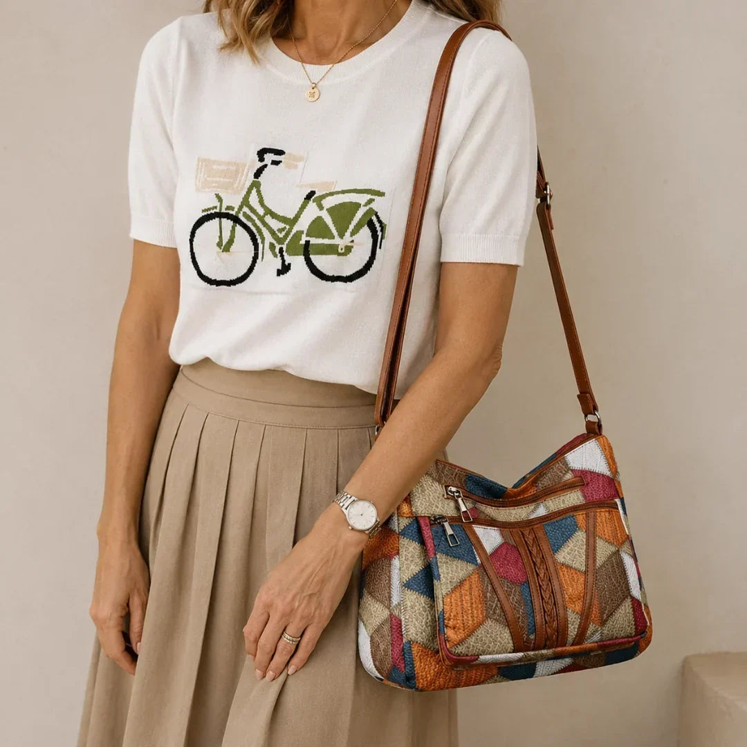 Woman wearing the patchwork shoulder bag on her arm with a white knitted top and beige pleated skirt. 1