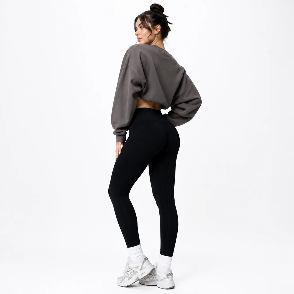 Model in black high-waisted leggings and a grey cropped sweatshirt, turned away to show the rear, with white trainers. 4