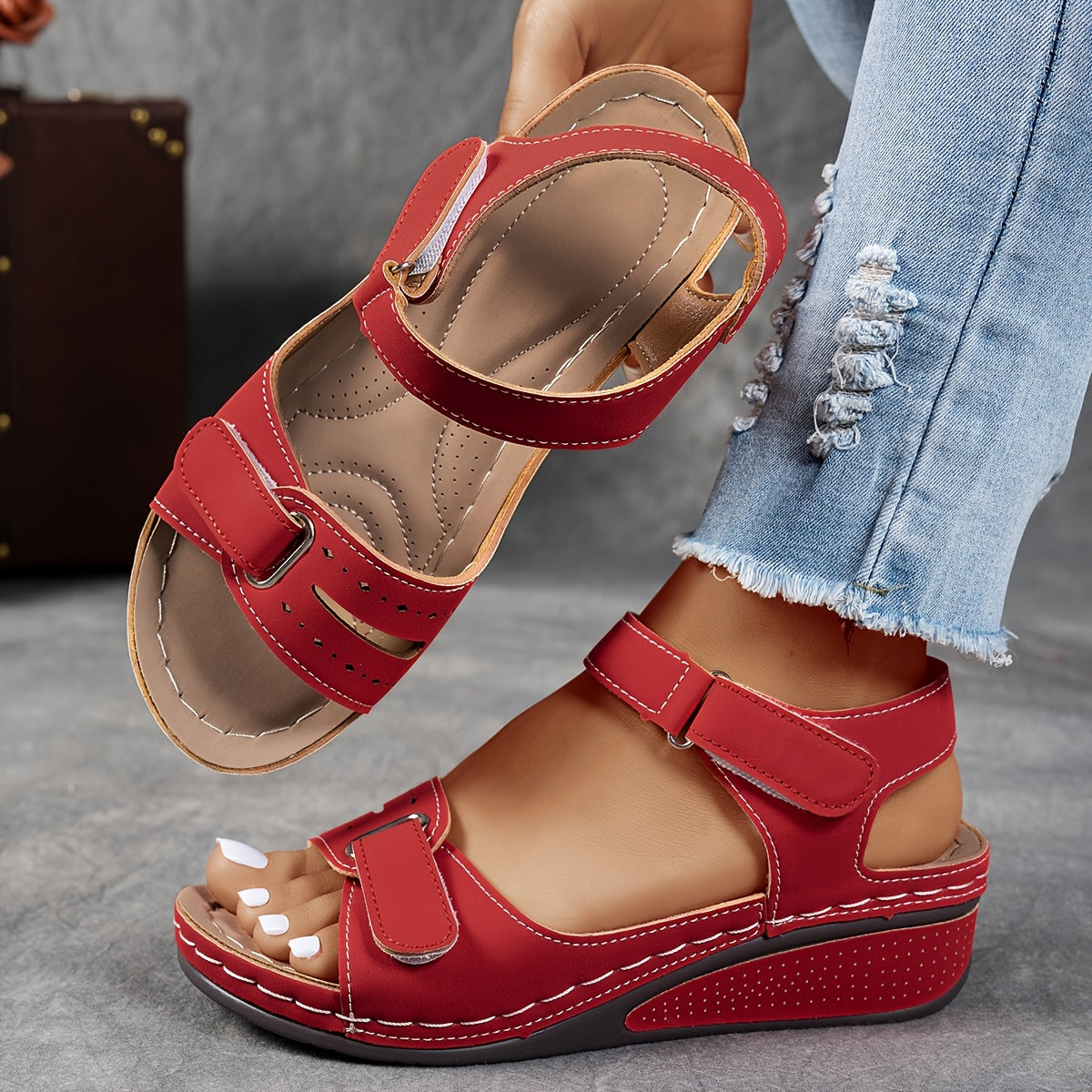 Red wedge sandals with contrast stitching, one worn with ripped jeans and the other held up to show the padded insole. 2