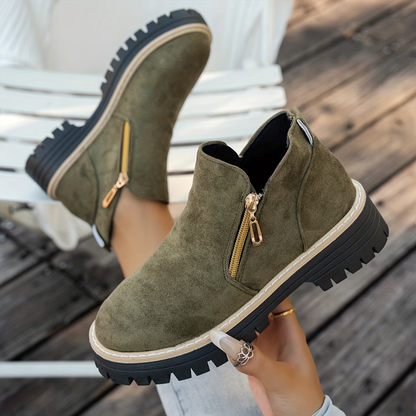 Olive green suede-look ankle boots with gold side zips and chunky treaded soles, worn by a model on decking. 3