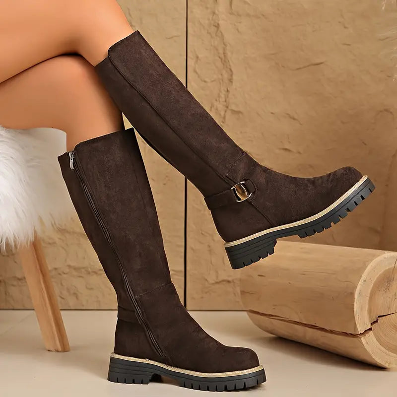 Dark brown suede-look tall boots worn by a model with crossed legs, showing the side zip, buckle and lugged black sole. 5