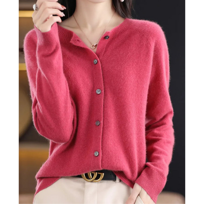 Model wearing the button-up round-neck cardigan in raspberry pink, hand raised to the collar, with a black belt and cream trousers. 1