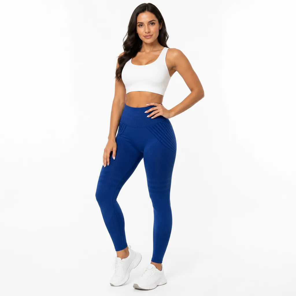 Front view of a smiling model in royal blue high-waisted leggings with a white sports bra and white trainers. 26