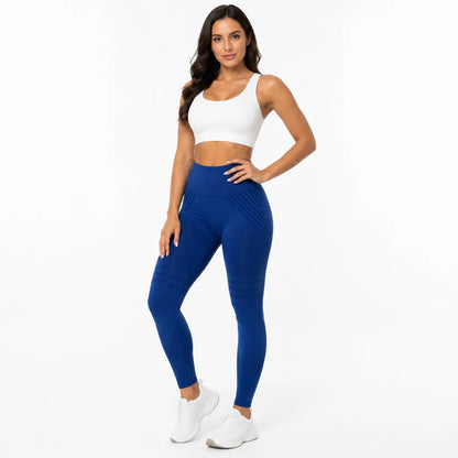 Front view of a smiling model in royal blue high-waisted leggings with a white sports bra and white trainers. 26