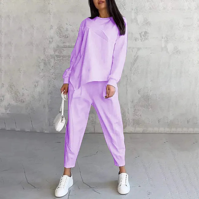 Model wearing the lilac set, standing front-on with a small white bag and white trainers on a grey floor. 4