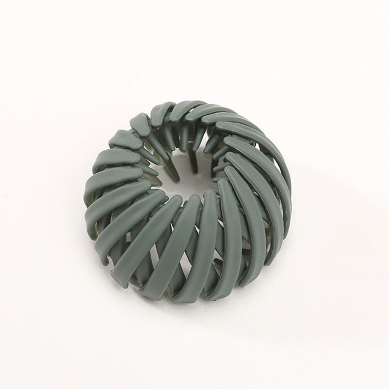 Single matte sage green spiral bird's-nest clip on a plain pale background, seen from above with the central opening visible. 9