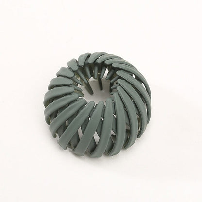 Single matte sage green spiral bird's-nest clip on a plain pale background, seen from above with the central opening visible. 15