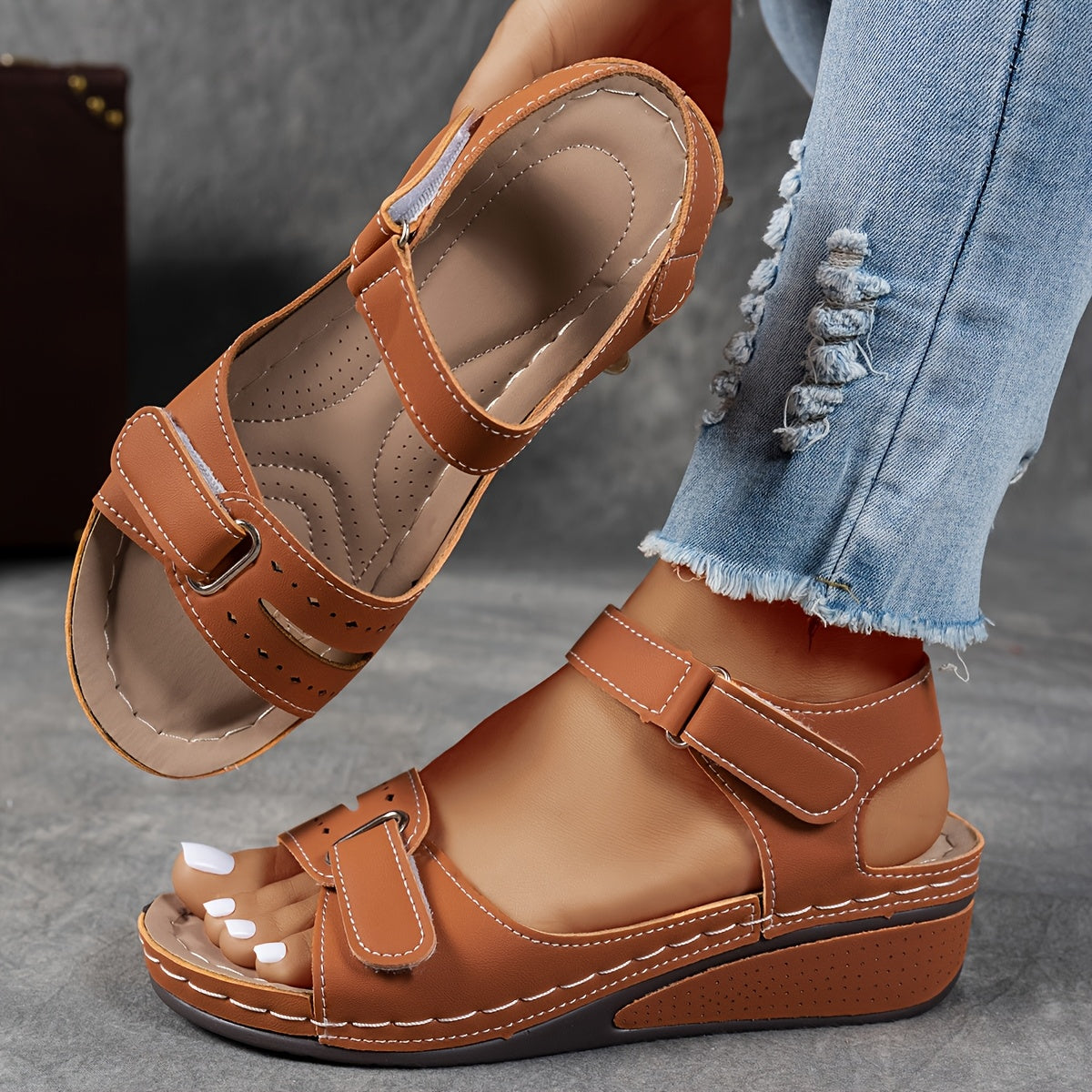 Tan-brown wedge sandals with hook-and-loop straps, one worn with frayed denim and one raised to show the contoured footbed. 5
