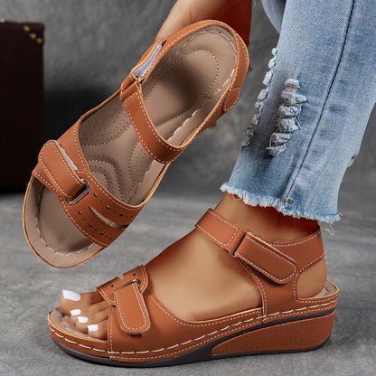 Tan-brown wedge sandals with hook-and-loop straps, one worn with frayed denim and one raised to show the contoured footbed. 5