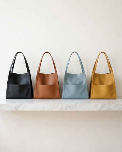 Four tote bags in black, tan, light blue and mustard yellow lined up side by side on a white marble shelf. 5