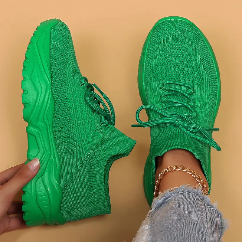 Top-down view of vivid green knit sneakers with matching chunky green soles, one held in a hand and one worn. 19