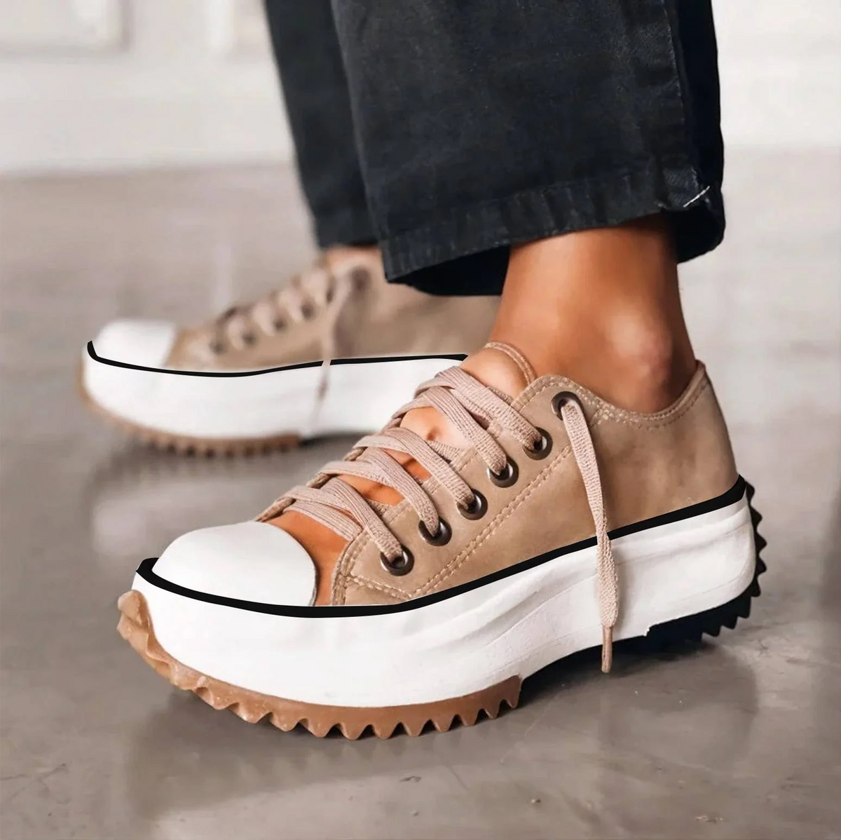 Side view of beige lace-up trainers with a chunky white platform sole and zigzag gum tread, worn with dark trousers. 1