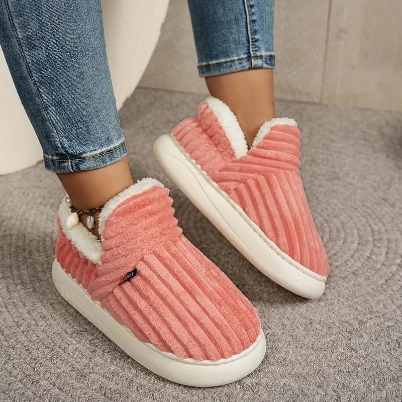 Coral pink ribbed slippers worn by a model in jeans, shown at an angle on a woven rug. 12