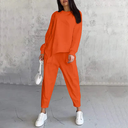 Model wearing the bright orange set, front view, holding a small white bag and wearing white trainers. 5