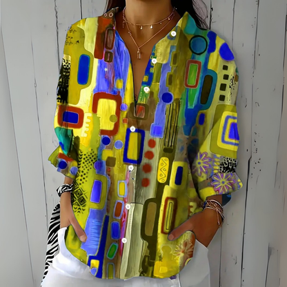Model wearing the blouse in a yellow and olive colourway with blue and purple abstract shapes, with sleeves rolled to the forearm. 5