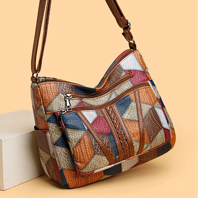 Patchwork bag angled on a pale block against a peach background, showing zipped front pockets and plaited faux leather trim. 4