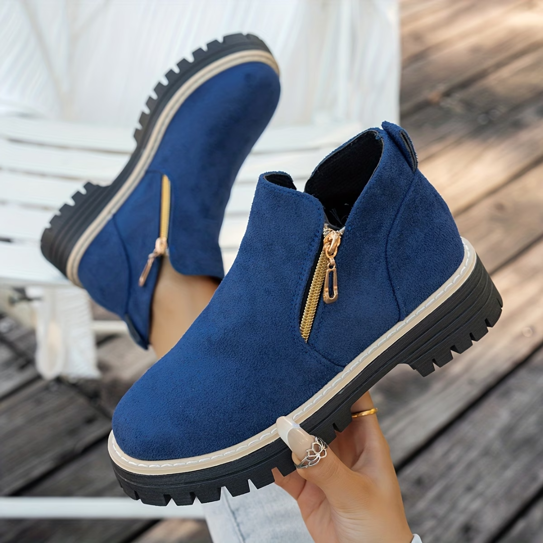 Navy blue suede-look ankle boots with gold side zips and chunky treaded soles, worn by a model on wooden decking. 6