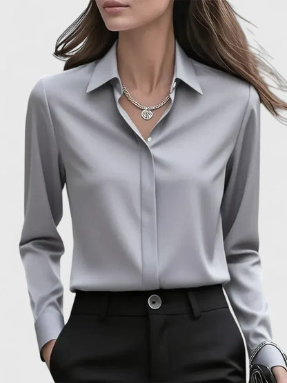 Front view of the grey satin blouse on a model, with collar and hidden placket, worn tucked into black trousers with a large button. 4