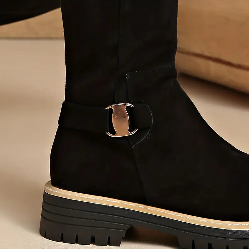 Close-up of the black boot's ankle strap with gold-tone metal buckle above the chunky ridged sole with contrast stitching. 3