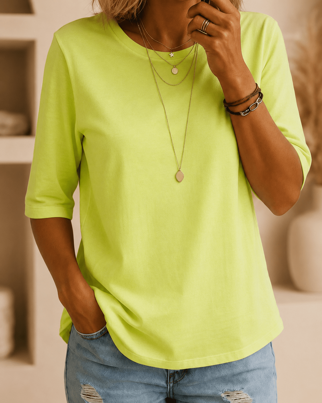 Model wearing the neon green tee with layered gold necklaces, bracelets and light blue ripped jeans, one hand in a pocket. 1