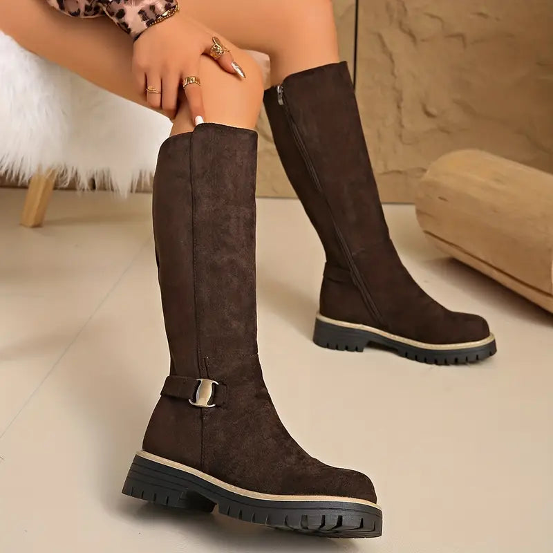 Model seated in dark brown knee-high boots, one boot showing the buckle strap, the other the full-length side zip. 6