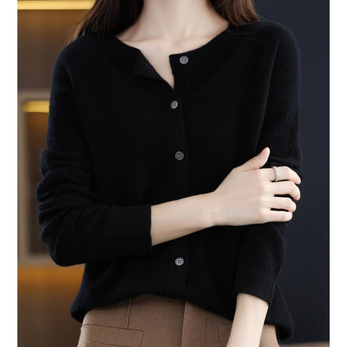 Black cardigan worn by a model with arm folded across her body, grey buttons contrasting with the dark knit, over camel trousers. 6