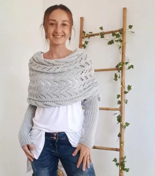 Pale grey wrap with soft cowl neckline and ribbed sleeves, model smiling beside a ladder with fairy lights. 15