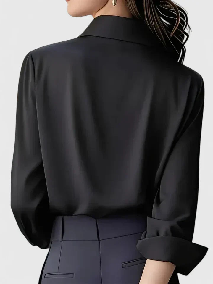 Back view of the black blouse on a model, showing the smooth back, folded-back cuff and collar, worn with dark trousers. 5